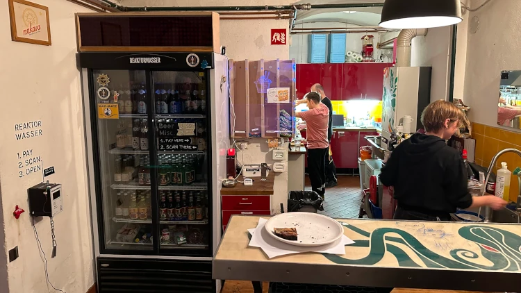 A glass-front fridge carrying beverages with a box of stacked ramen packages next to it